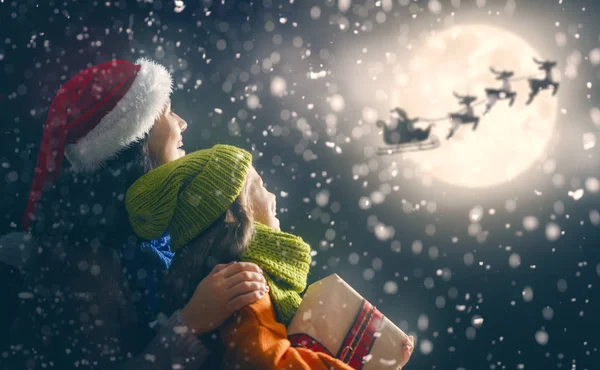 圣诞快乐 节日愉快 可爱的小孩子与母亲 圣诞老人在雪橇上飞向月亮的天空 家庭在黑暗的背景享受假日 — 图库照片