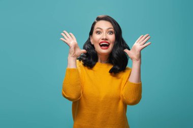 Güzel genç kadın sarı kazaklı turkuaz arka plan üzerinde poz şaşırttı.