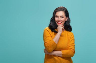 Sarı kazaklı turkuaz arka plan üzerinde poz neşeli güzel ve genç birbayan.