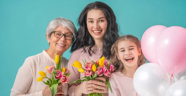 幸せな女性の日 子娘は ママとおばあちゃんの黄色の花チューリップを与えて祝福です おばあちゃん ママと女の子笑顔と光を抱いてブルーの背景 家族の休日と一体感 — ストック写真