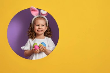 Tavşan kulakları Paskalya gününde giyen sevimli küçük çocuk. Parlak mor ve Sarı zemin üzerine boyalı yumurta ile kız. 