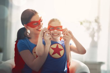 Anne ve çocuğu birlikte oynama. Kız ve anne süper kahraman kostümü içinde. Anne ve çocuk eğlence gülümseyen ve sarılma. Aile tatili ve beraberlik.