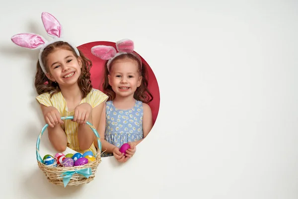 イースターの日にバニーの耳を着てかわいい小さな子供 白とピンクの背景に塗られた卵を持つ女の子 — ストック写真