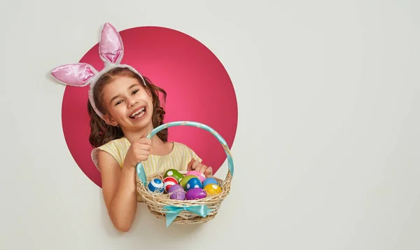 イースターの日にバニーの耳を着てかわいい小さな子供 ピンクと白の背景に塗られた卵を持つ少女 — ストック写真