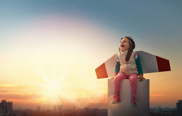 Little child playing pilot. Girl on the background of sunset sky. Kid in an astronaut costume dreaming of becoming a spaceman.