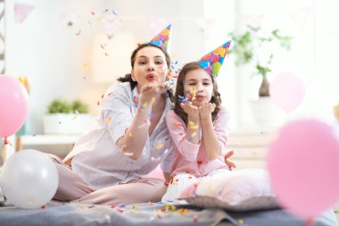 Komik zaman. Anne ve küçük kızı evde oynuyorlar. Kızlar konfeti atıyor. Aile tatili ve birliktelik.