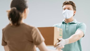 Tıbbi lastik eldivenli ve maskeli teslimatçı. İnternetten alışveriş. Karantinaya alın. Kuryeden kutu kabul eden kadın.