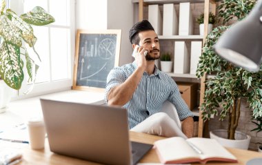 Evde dizüstü bilgisayarla çalışan mutlu bir genç adam..