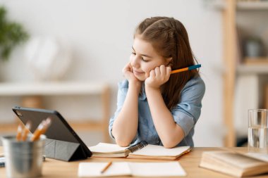 Okula dönelim. Mutlu çocuk masada oturuyor. Ödev yapan ya da online eğitim alan kız.