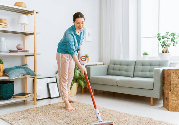 Happy woman vacuuming the room. Housewife doing the cleaning in the house.