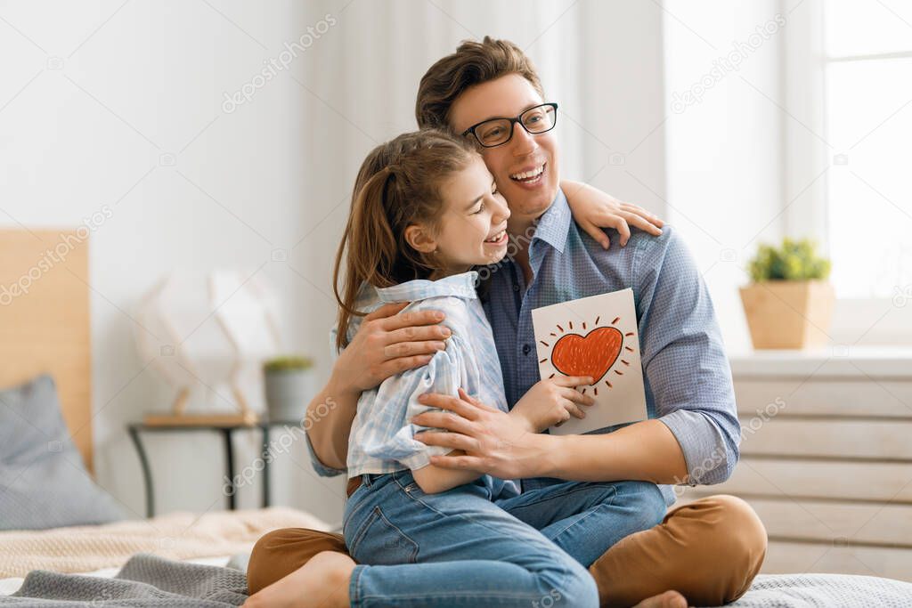 Happy father's day! Child daughter congratulating dad and giving him postcard. Daddy and girl smiling and hugging. Family holiday and togetherness.