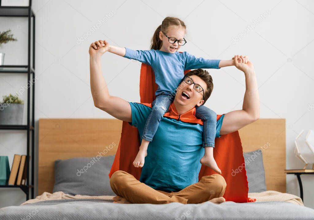 Father and his child playing together. Girl and dad in Superhero costume. Daddy and kid having fun, smiling and hugging. Family holiday and togetherness.