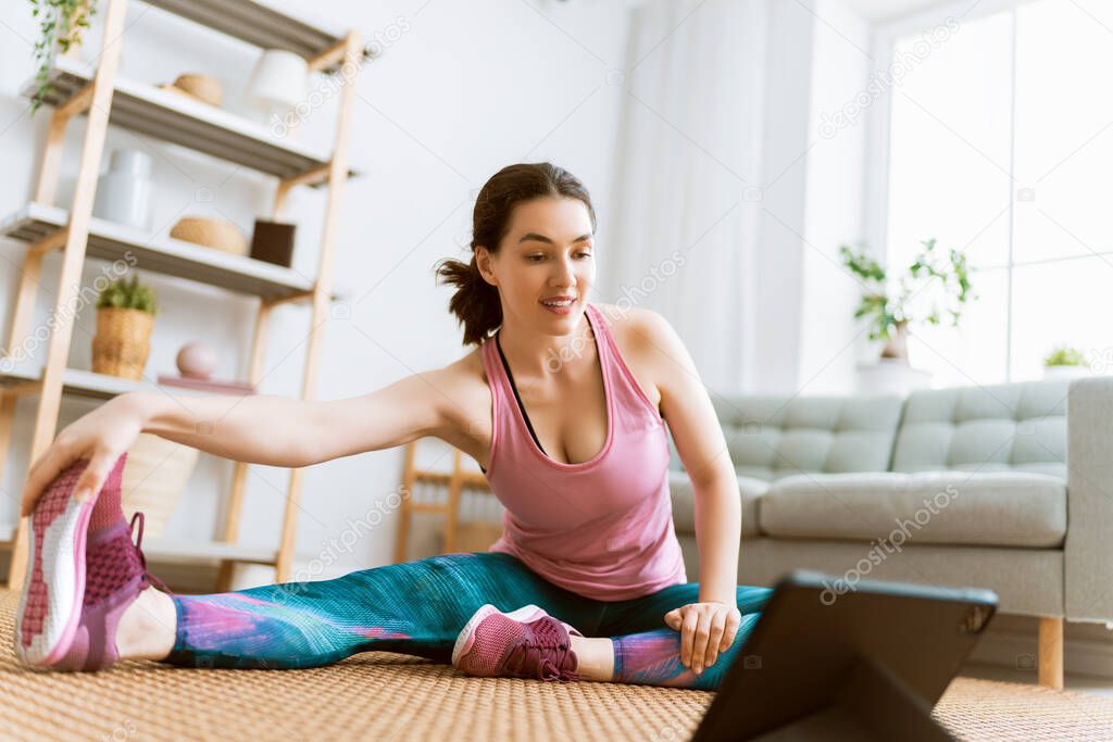 Young woman in activewear watching online courses on tablet while exercising at home.