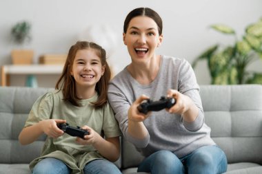 Mutlu aile birlikte. Anne ve kız çocuğu video oyunu oynuyorlar. İnsanlar evde eğleniyor..