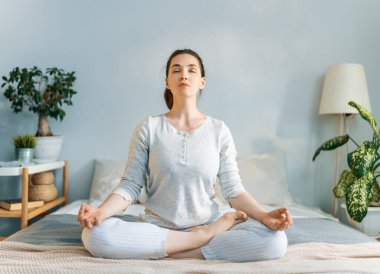 Mutlu genç kadın güneşli bir sabahın tadını çıkarıyor ve yatakta meditasyon yapıyor..