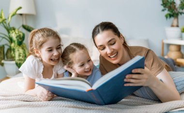 Sevgi dolu bir aile. Güzel genç anne, kızlarına evde, yatakta kitap okuyor..