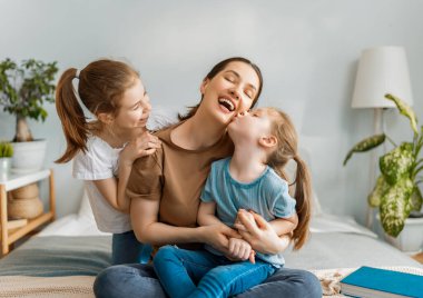 Güzel kızlar ve anneleri güneşli sabahların tadını çıkarırlar. Evde iyi eğlenceler. Aile yatak odasında yatakta oynuyor..