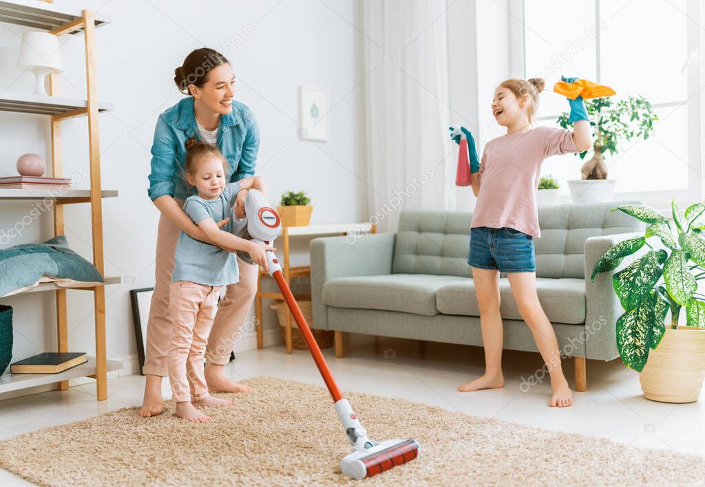 Happy family vacuuming the room. Mother and daughters doing the cleaning in the house.