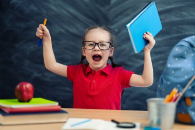 Okula dönün! Mutlu, sevimli, çalışkan çocuk kapalı bir masada oturuyor. Çocuk sınıfta tahtada öğreniyor..