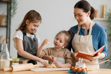 Mutlu aile birlikte fırın hazırlıyor. Anne ve çocuk kızları kurabiye pişiriyor ve mutfakta eğleniyorlar. Ev yapımı yemek ve küçük bir yardımcı.. 