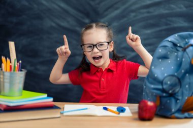 Okula dönün! Mutlu, sevimli, çalışkan çocuk kapalı bir masada oturuyor. Çocuk sınıfta tahtada öğreniyor..