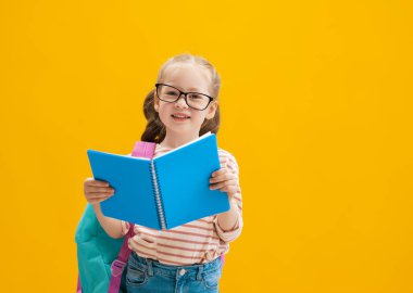 Okula dön ve mutlu ol! Renkli duvar arka planında sevimli, çalışkan bir çocuk. Sırt çantalı çocuk. Kız çalışmaya hazır..