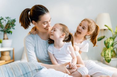 Güzel kızlar ve anneleri güneşli sabahların tadını çıkarırlar. Evde iyi eğlenceler. Aile yatak odasında yatakta oynuyor..