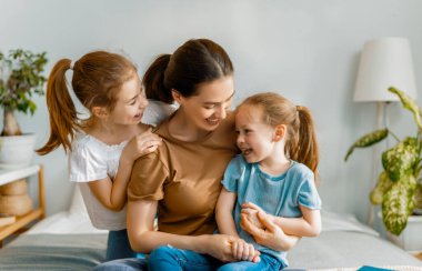 Güzel kızlar ve anneleri güneşli sabahların tadını çıkarırlar. Evde iyi eğlenceler. Aile yatak odasında yatakta oynuyor..