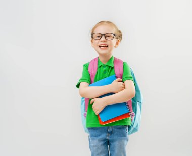 Okula dön ve mutlu ol! Beyaz duvar arka planında sevimli, çalışkan bir çocuk. Sırt çantalı çocuk. Kız çalışmaya hazır..