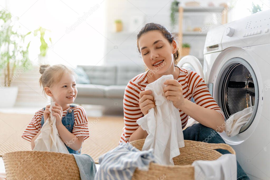 Beautiful young woman and child girl little helper are having fun and smiling while doing laundry at home.