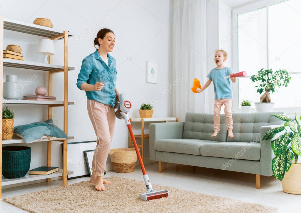 Happy family vacuuming the room. Mother and daughter doing the cleaning in the house.