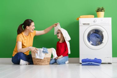 Güzel genç kadın ve kız çocuk küçük yardımcı evde çamaşır yıkarken eğleniyor ve gülümsüyor..