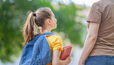 Ortaokulun ebeveyni ve öğrencisi el ele gidiyor. Sırt çantalı kadın ve kız. Dersler başlıyor. Sonbaharın ilk günü.
