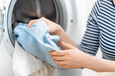 Kadın evde çamaşır yıkıyor. Çamaşır makinesi ve eller kapalı.