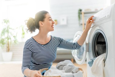 Beautiful young woman is smiling while doing laundry at home. clipart