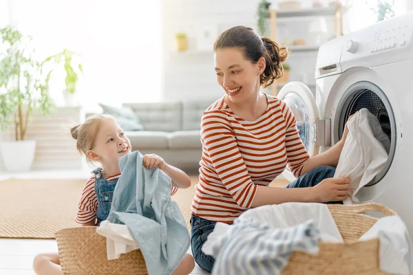 美しい若い女性と子供の女の子の小さなヘルパーは家で洗濯をしながら楽しさと笑顔を持っています — ストック写真