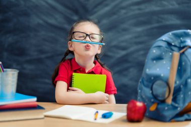 Okula dönün! Mutlu, sevimli, çalışkan çocuk kapalı bir masada oturuyor. Çocuk sınıfta tahtada öğreniyor..