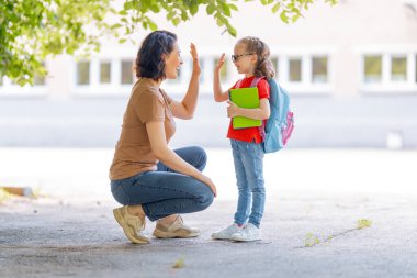 İlkokulun ebeveynleri ve öğrencileri el ele gider. Sırt çantalı kadın ve kız. Dersler başlıyor. Sonbaharın ilk günü.