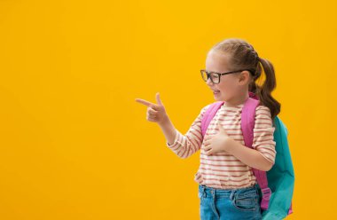 Okula dön ve mutlu ol! Renkli duvar arka planında sevimli, çalışkan bir çocuk. Sırt çantalı çocuk. Kız çalışmaya hazır..