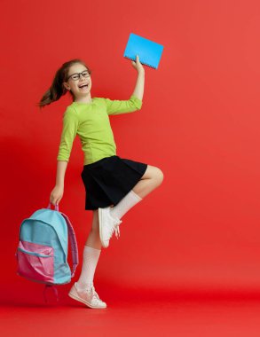 Okula dön ve mutlu ol! Renkli duvar arka planında sevimli, çalışkan bir çocuk. Sırt çantalı çocuk. Kız çalışmaya hazır..