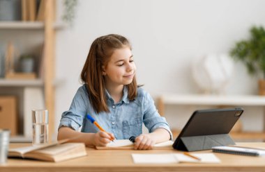 Okula dönelim. Mutlu çocuk masada oturuyor. Ödev yapan ya da online eğitim alan kız.