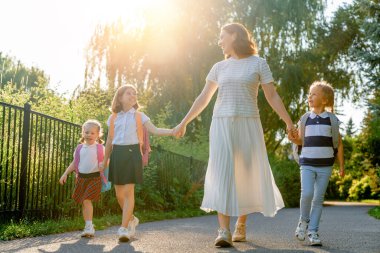 İlkokulun ebeveynleri ve öğrencileri el ele. Sırt çantalı kadın ve kızlar. Dersler başlıyor. Sonbaharın ilk günü.