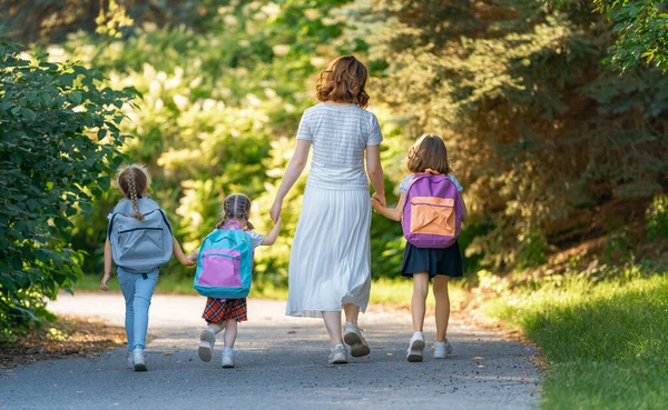 父母和小学生是紧密联系在一起的 背着背包的女人和女孩开始上课 秋天的第一天 — 图库照片