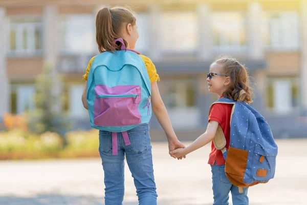 Pupils of primary school. Girls with backpacks outdoors. Beginning of lessons. First day of fall.