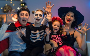 Anne, baba ve çocukları evde eğleniyorlar. Cadılar Bayramı 'nı kutlayan mutlu aile. İnsanlar karnaval kostümü ve makyaj yapıyor..