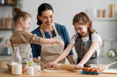 Mutlu aile birlikte fırın hazırlıyor. Anne ve çocuk kızları kurabiye pişiriyor ve mutfakta eğleniyorlar. Ev yapımı yemek ve küçük bir yardımcı.. 