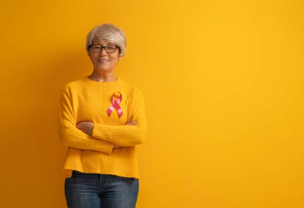 有黄色背景的老年妇女 粉色丝带就像乳腺癌意识的象征 支助患肿瘤的人 — 图库照片