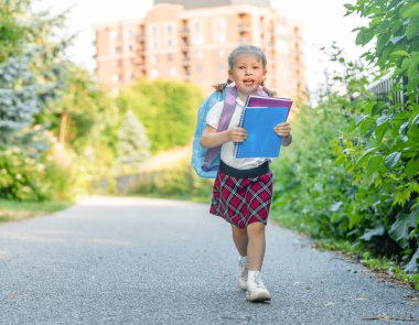 Elinde kitapla ilkokul öğrencisi. Açık hava binasının yakınında sırt çantalı bir kız. Dersler başlıyor. Sonbaharın ilk günü.
