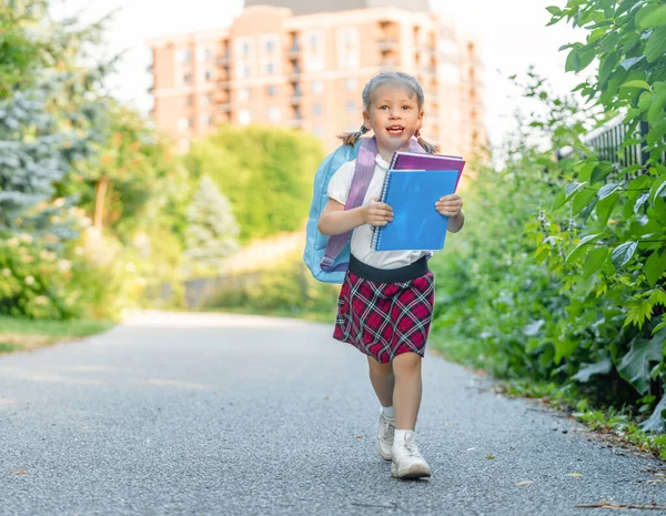 小学生手里拿着一本书 在室外建筑附近背着背包的女孩 开始上课 秋天的第一天 — 图库照片