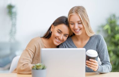 Laptop kullanan iki mutlu genç kadın. Arkadaşlar birlikte vakit geçiriyorlar..